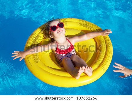 Funny little girl swims in a pool in an yellow life preserver