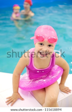 Funny little girl sitting near  swimming  pool in an pink life preserver