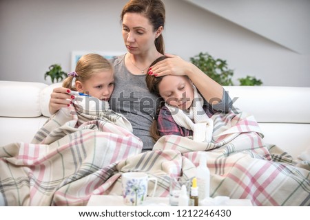 mother sits on the couch with 2 sick daughters and measures the temperature