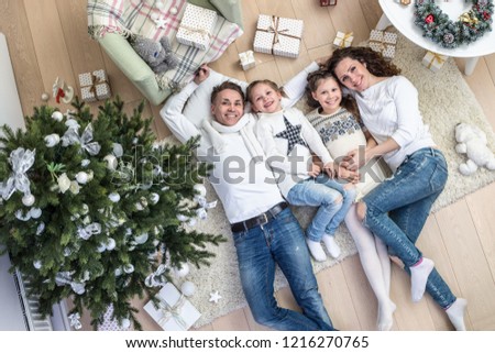 Happy family with two children lies under the Christmas tree with gifts on the carpet. View from above