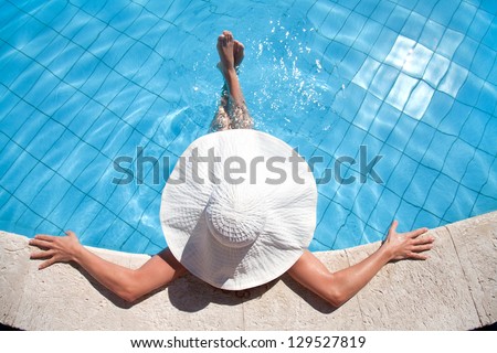 Unrecognizable woman in big hat relaxing on the swimming pool