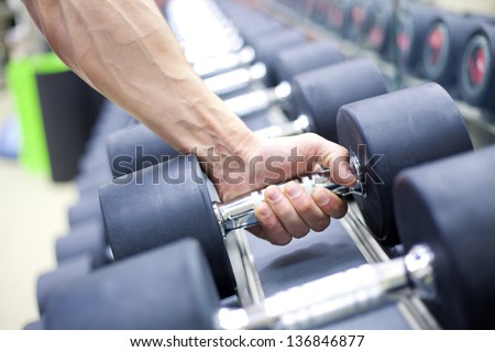 strong man\'s hand takes a heavy dumbbell in gym