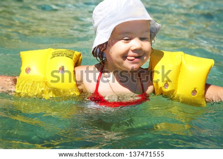 Funny little girl swims in a pool in yellow inflatable armbands