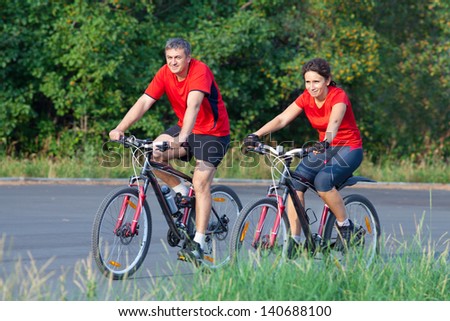 happy mature couple riding a bicycle in the green park