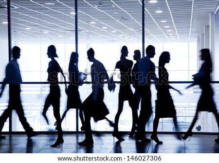 silhouettes of business people rushing for the large windows in the background