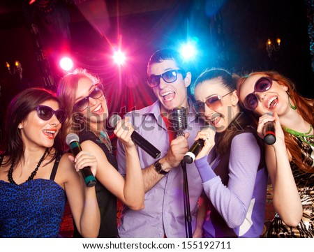 group of young people singing into  microphone at  party. karaoke