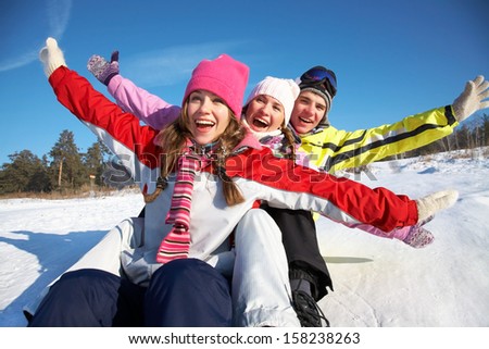 Group Of Teenagers Slide Downhill In Wintertime