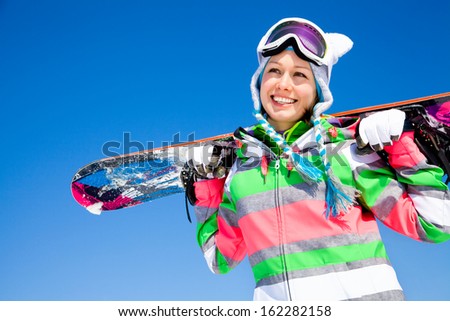Portrait Of Young Smiling Woman With Snowboard On Ski Holiday In Mountains