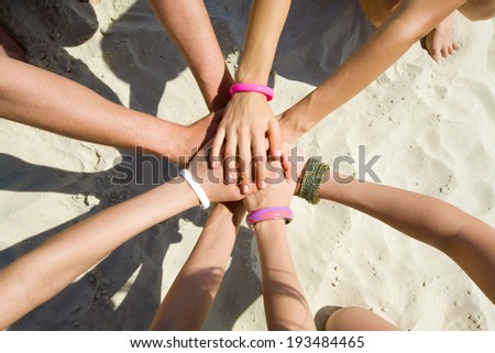 hands of young people stretching to the center on beach