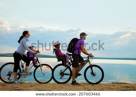Young family with two kids go for a cycle ride on the beach at background sunset