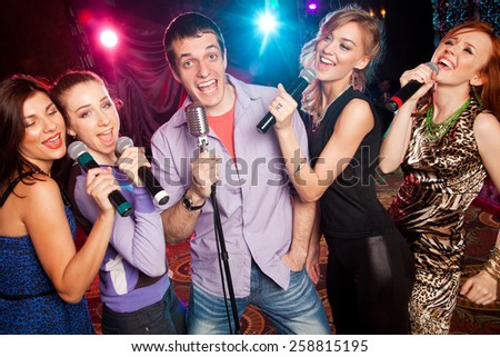 group of young people singing into  microphone at  party. karaoke