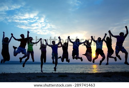large group of young people having fun and jumping on the beach at sunset