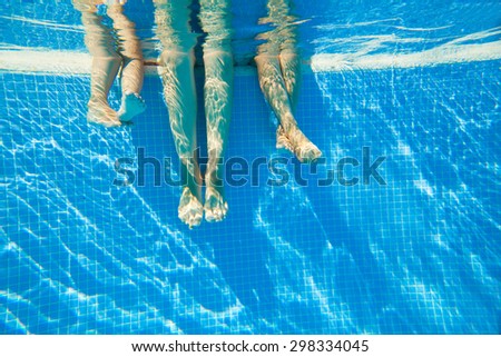 3 pairs of feet under water in a swimming pool