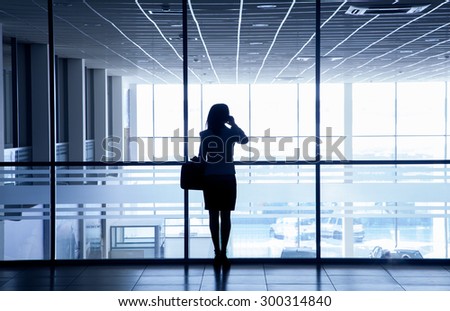 Silhouette of a woman standing alone against the backdrop of large windows office