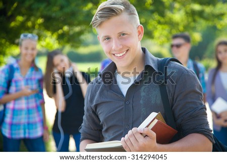 young  student with books on the background of his friends in the green park