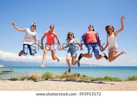 group of happy young people jumping at the beach on beautiful summer day