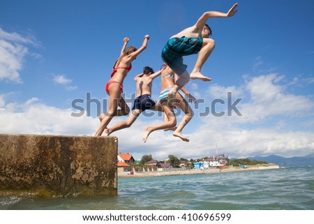 Group of teenagers jumping off the pier into the sea. fun summer vacation