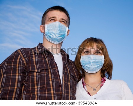 Couple wearing flu masks looks forward against the blue sky