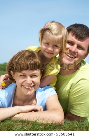 family lifestyle portrait of a mum and dad with their daughter having good time on the green grass