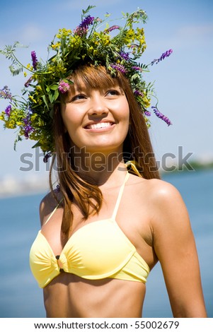 Portrait of Young beautiful woman in a wreath of wild flowers on the sea