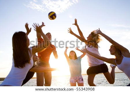group of young people playing volleyball on the beach