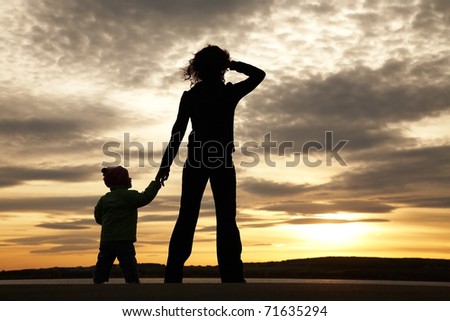 Silhouette of mother and baby looking away into the sunset and water