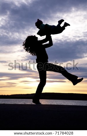 Silhouette of mother which turns the child against a sunset and water