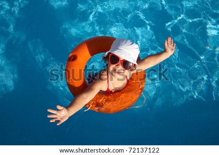 Funny little girl swims in a pool in an orange life preserver