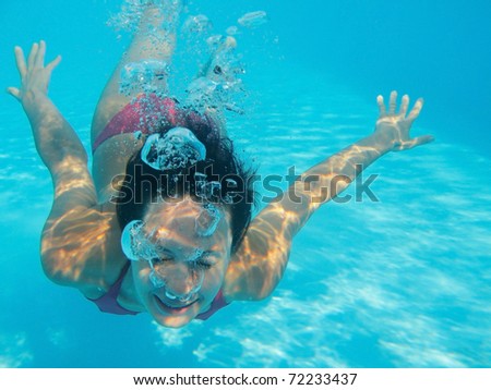 Woman swimming underwater in pool smiling. Young female swimmer  at holiday resort.