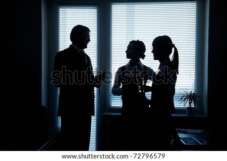 silhouettes of business partners discuss against the window in the office