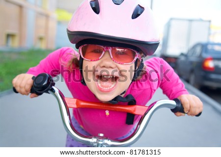 Portrait of a playful funny girl in a pink safety helmet on her bike