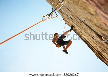 silhouette of rock climber climbing an overhanging cliff against the blue sky