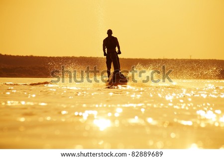 strong man drives on the jetski above the water at sunset .silhouette spray.