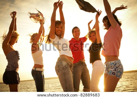 group of happy young people dancing at the beach on  beautiful summer sunset