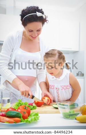 Pregnant mother and daughter in kitchen making a salad