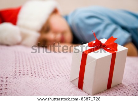 The young boy sleeps on bed and before it there is a beautiful Christmas gift