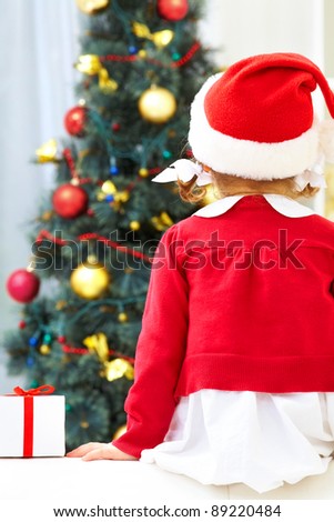 Little girl sitting against Christmas tree. Back view