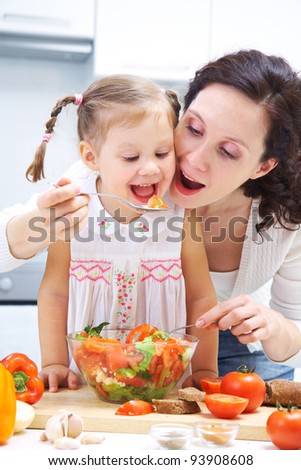 Mother and daughter eating vegetables saladr in kitchen