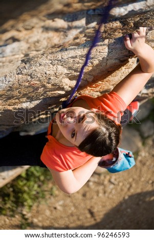 The beautiful girl is engaged in rock-climbing on a vertical rock