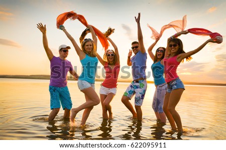 Young fun people enjoying summer on the beach at sunset