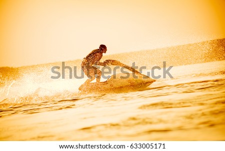 young man drive on the jet ski above the water at sunset .silhouette. spray.
