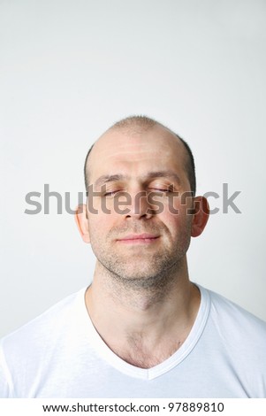 Portrait of positive bald-headed man with closed eyes on white background