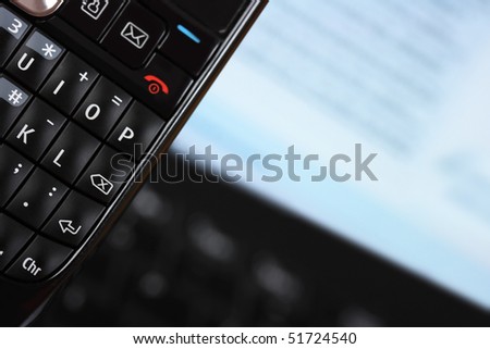 Close-up of mobile phone keypad with laptop in background