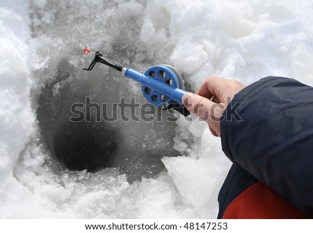 Hand holding ice fishing rod and and angling from a hole in the ice