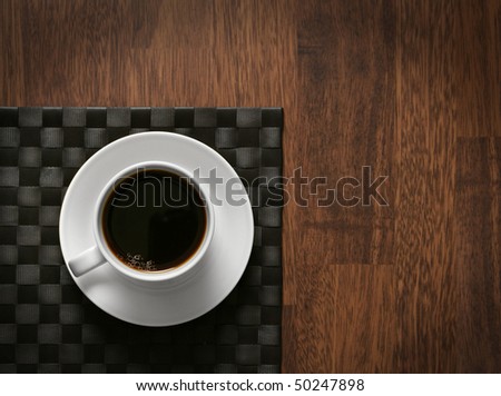 Steaming hot cup of black coffee on wooden table and dark tablemat