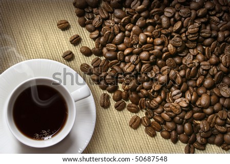 Roasted coffee beans and steaming hot coffee cup on burlap background