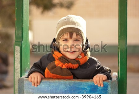 The boy in a cap and in a scarf goes for a drive on a swing