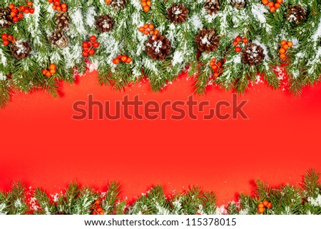 Christmas green  framework, postcard with snow, cones and holly berry  isolated on red paper background