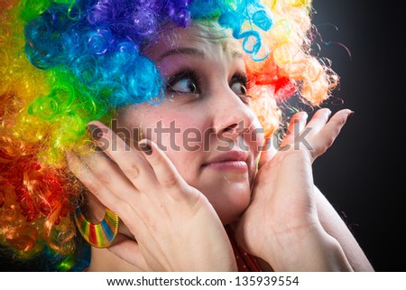 young beauty woman in multicolored clown wig smiling on black background