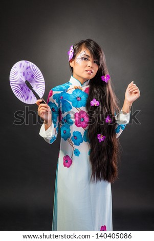 Beautiful asian woman wears a national dress is holding a fan, isolated on a black background